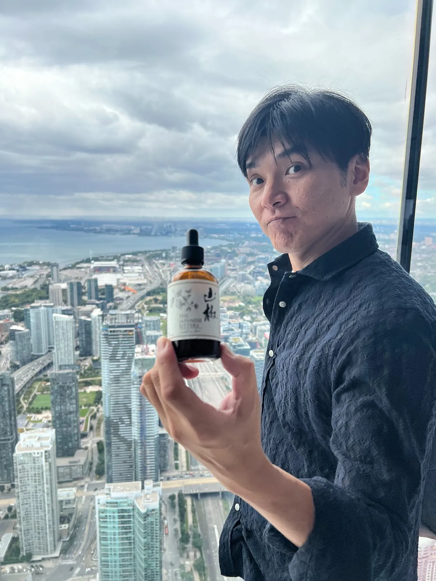Yuki Yamazaki of The Japanese Bitters holding a bottle of Sansho bitters at the CN Tower, Toronto